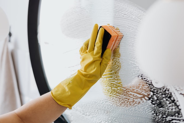 Cropped image of someone wearing yellow gloves using a sponge to clean a bathroom mirror